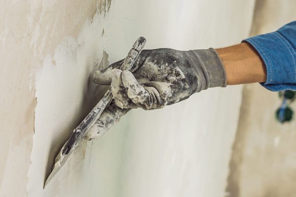master is applying white putty on a wall and smearing by putty knife in a room of renovating house in daytime. BANNER, long format