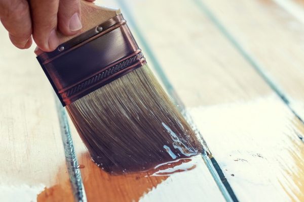 Brush in hand. Close up of covering wooden surface with acryl lacquer.